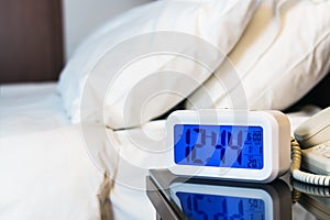 Alarm clock electronic stands on a bedside table near the bed