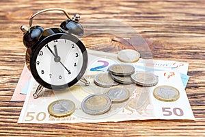 Alarm clock with euro bills and coins on the wooden table. Business concept