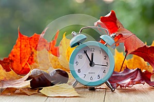 Alarm clock and fallen autumn leaves. Autumn season concept. Time change concept