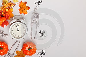 Alarm clock with fallen leaves pumpkins skeletons spiders. Transitional change of autumn time, change of seasons halloween