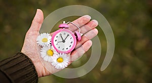 Alarm clock and flowers in a hand, daylight savings time or spring, summer banner