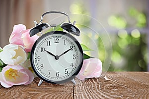 Alarm clock and flowers on table against background. Spring time