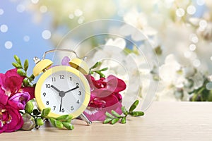 Alarm clock and flowers on wooden table against background, space for text. Spring time