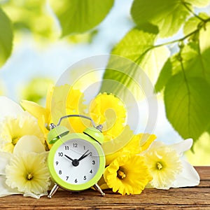 Alarm clock and flowers on wooden table against blurred background. Spring time