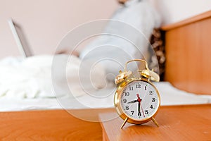 Alarm clock on foreground and business man or woman sitting in white bed working on the laptop computer on background