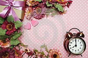 Alarm clock and gift box with roses bouquet on pink polka dot background