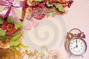 Alarm clock and gift box with roses bouquet with space copy on pink polka dot background
