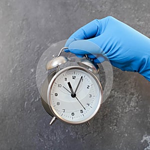 Alarm clock held by a hand in a medical glove on a gray background