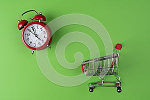 Alarm clock isolate on green background with a shopping trolley