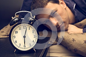 Alarm clock with male model in bed in background.