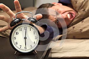 Alarm clock with male model in bed in background.