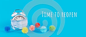 Alarm clock in medical mask and plastic balls as viruses on the blue background. Coronavirus pandemic reduction, moving