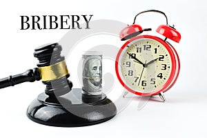 Alarm clock, money banknote and judge gavel over white background written with BRIBERY
