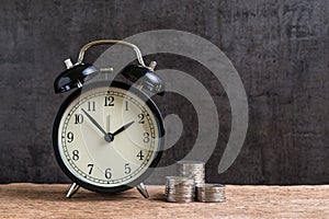 Alarm clock with money stack of coins on wooden table and black