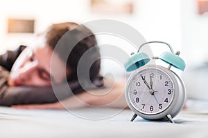 Alarm clock in the morning. Young man sleeps in the blurry background