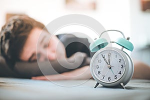 Alarm clock in the morning. Young man sleeps in the blurry background