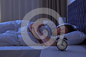 Alarm clock on nightstand near sleeping young man
