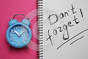 Alarm clock and notebook with text Don`t forget on pink background, flat lay. Reminder concept