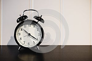 Alarm clock with 10 O`clock and twenty minuet, on black wooden table with white wall photo