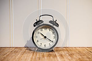 Alarm clock with 10 O`clock and twenty minuet, on wooden table and white wall photo