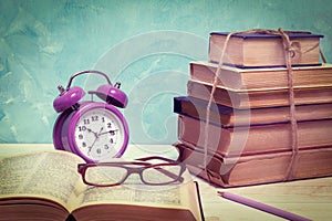Alarm clock, open book, glasses and a stack of old books tied with twine. Education and wisdom concept