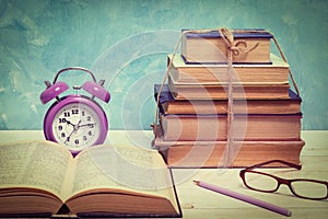 Alarm clock, open book, glasses and a stack of old books tied with twine. Education and wisdom concept