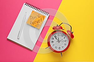 Alarm clock, pen, notebook and reminder note with phrase Don`t forget on color background, flat lay