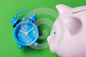 Alarm clock and piggy bank on a green background