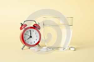 Alarm clock, pills and glass of water on background, close up