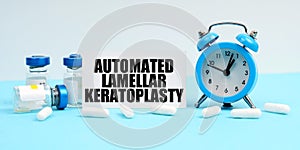 An alarm clock, pills, injections and a card with the inscription - Automated Lamellar Keratoplasty