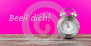 alarm clock with pink background with german text beeil dich, in english hurry up