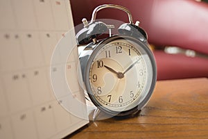 Alarm clock placed beside calendar on wooden table with window a
