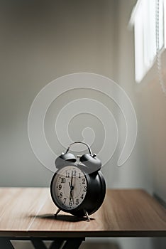 Alarm clock placed on table by the window, vertical image, copy area above.