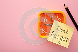 Alarm clock and reminder note with phrase Don`t forget on pink background