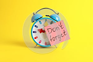 Alarm clock and reminder note with phrase Don`t forget on yellow background