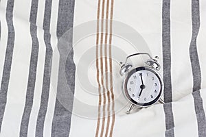 Alarm clock in retro vintage style, arrows on dial show 7 o`clock am on striped pillow in bed. Minimal modern style