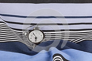 Alarm clock in retro vintage style, arrows on dial show 7 o`clock am on striped pillow in bed. Minimal modern style