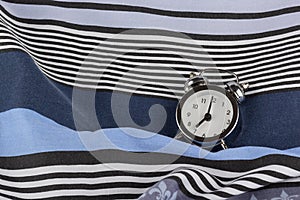 Alarm clock in retro vintage style, arrows on dial show 7 o`clock am on striped pillow in bed. Minimal modern style