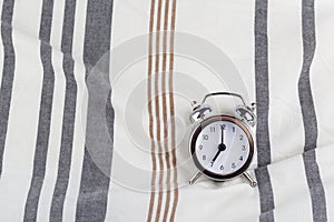 Alarm clock in retro vintage style, arrows on dial show 7 o`clock am on striped pillow in bed. Minimal modern style