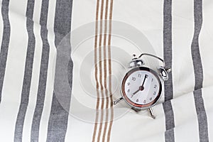 Alarm clock in retro vintage style, arrows on dial show 7 o`clock am on striped pillow in bed. Minimal modern style