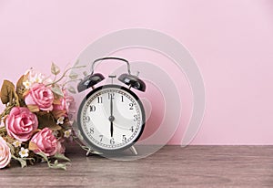 Alarm clock and rose on wood table with pink background and copy