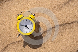 Alarm clock on the sand in the desert on a sunny day with a shadow