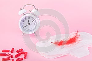 Alarm clock, a sanitary pad and painkillers on a pink background