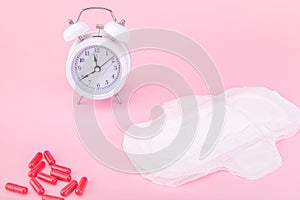 Alarm clock, a sanitary pad and painkillers on a pink background