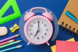 Alarm clock and school supplies on a blue background. The concept is time to get ready for school