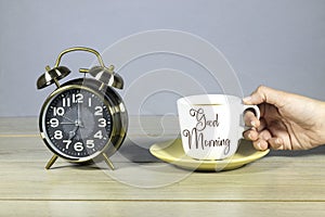 alarm clock showing 7 o`clock with woman hand drinking a cup of coffee with lettering good morning. ready for work concept