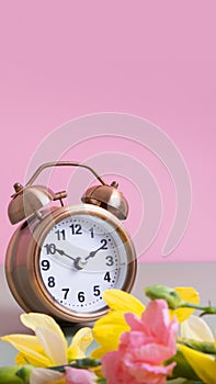 Alarm clock with spring flowers on color background. Spring time, daylight savings concept, spring forward. Copy space.
