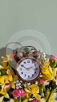 Alarm clock with spring flowers on color background top view, flat lay. Daylight savings concept, spring forward