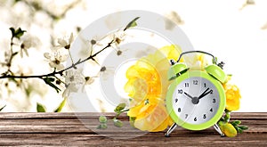 Alarm clock and spring flowers on wooden table, space for text. Time change