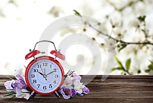 Alarm clock and spring flowers on wooden table, space for text. Time change